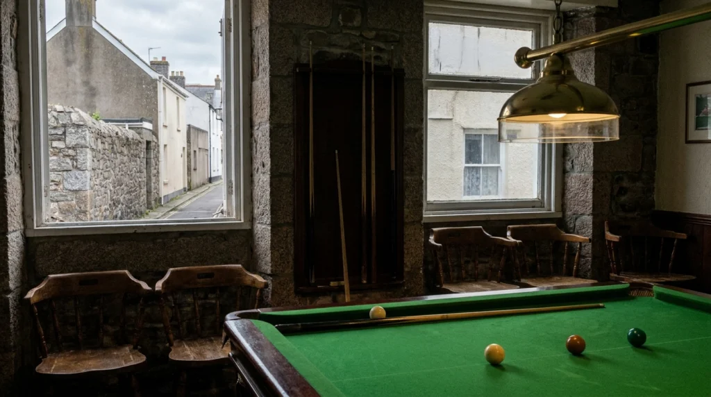 A green baize snooker table inside a traditional club room, lit by a low-hanging overhead light, with a few cues resting in a